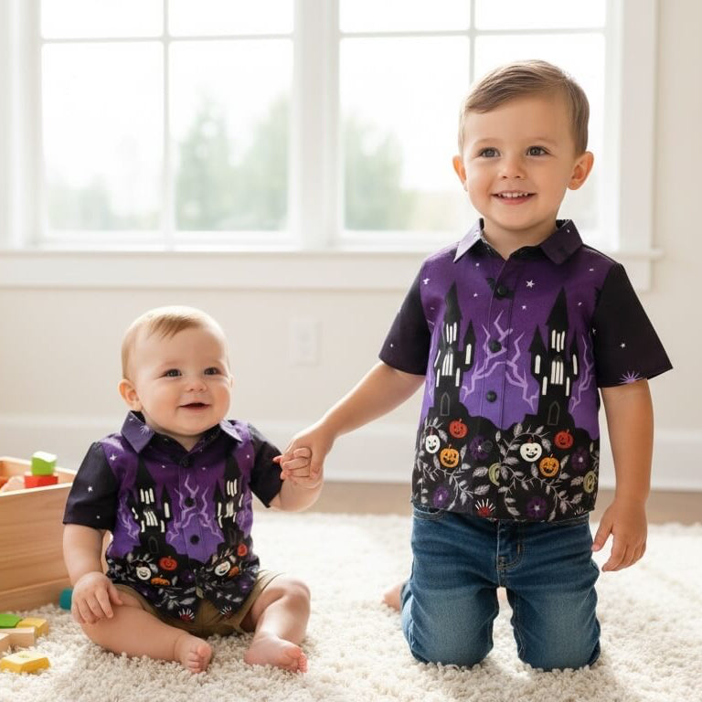 Two children wearing matching purple and black Halloween-themed short-sleeve button-up shirts with a haunted house and spider graphics.