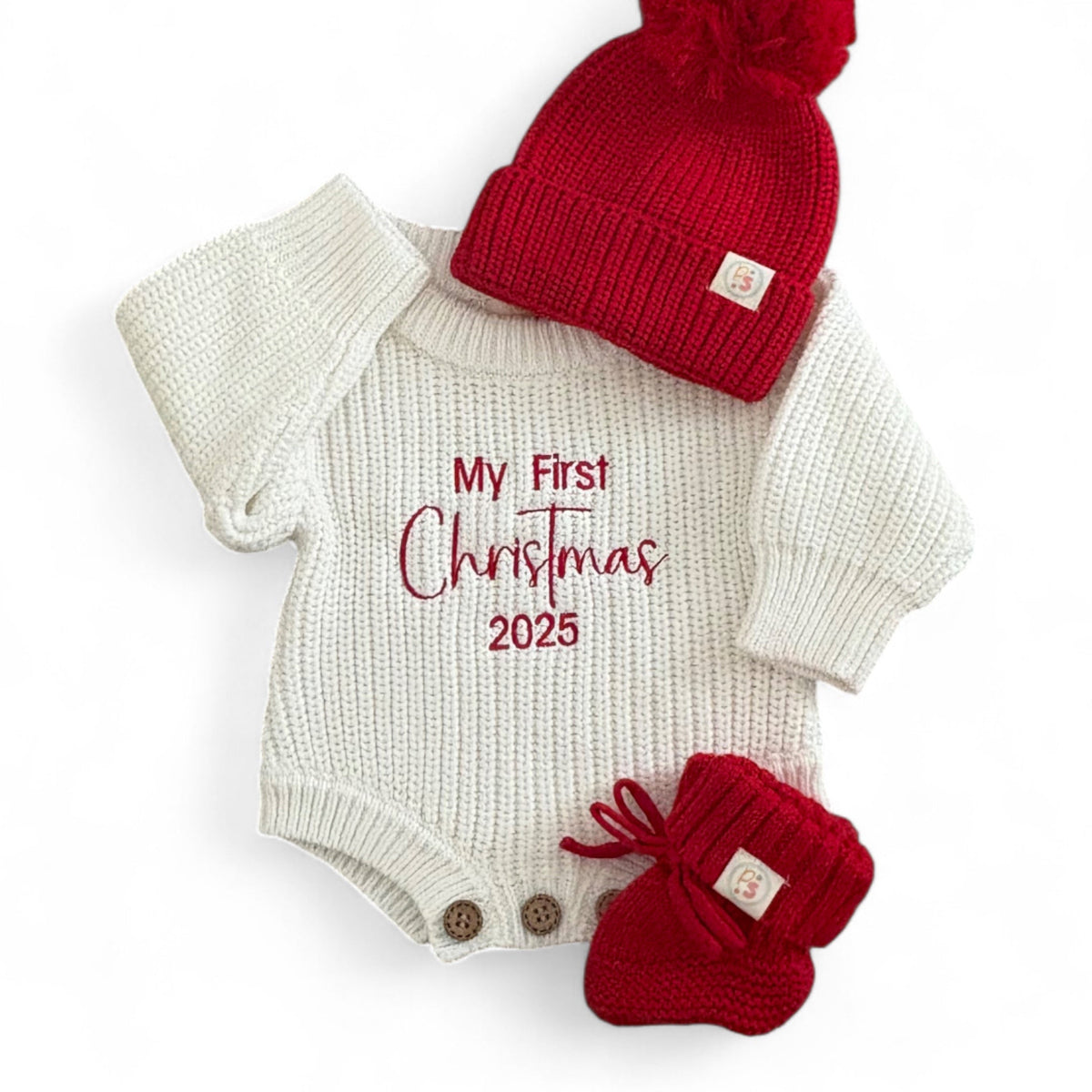 Baby onesie with 'My First Christmas 2025' text, red hat, and booties on a white background