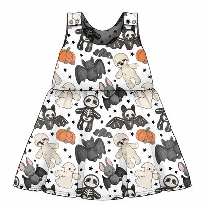 A sleeveless tiered dress with a white background and a Halloween-themed print featuring cartoon bats, skeletons, ghosts, teddy bears, and pumpkins.