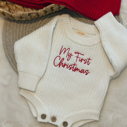 An off-white textured knit baby romper with 'My First Christmas' embroidered in red script across the chest.