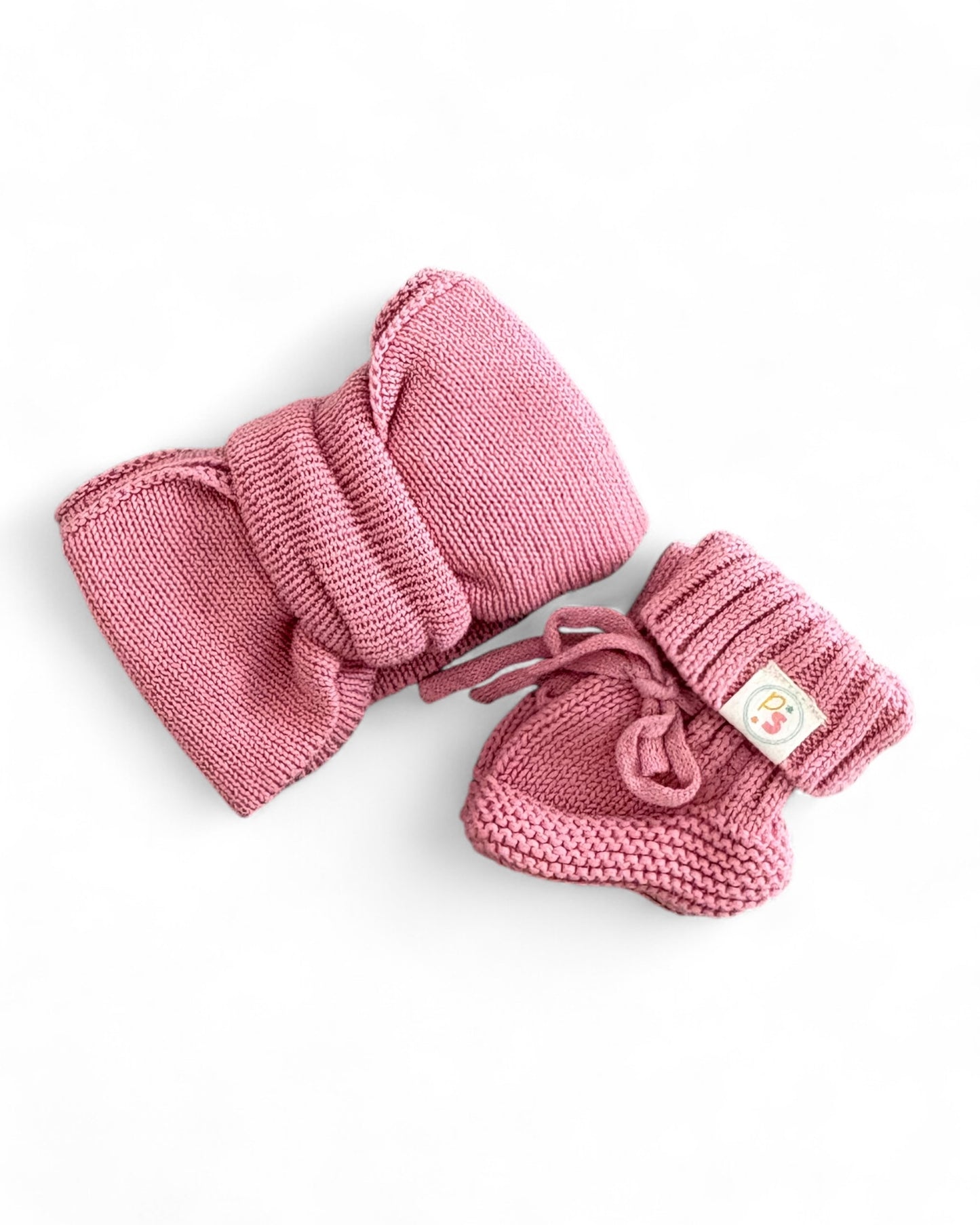 Pink knitted baby headband and booties set on a white background