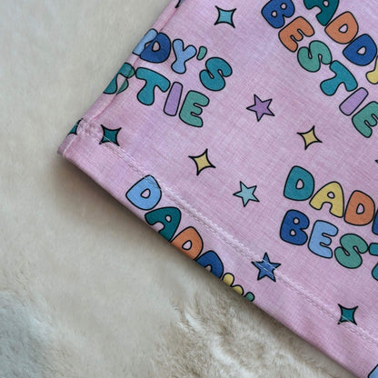 A close-up of a pink tshirt featuring a colourful print with the words 'Daddy's Bestie' and stars.