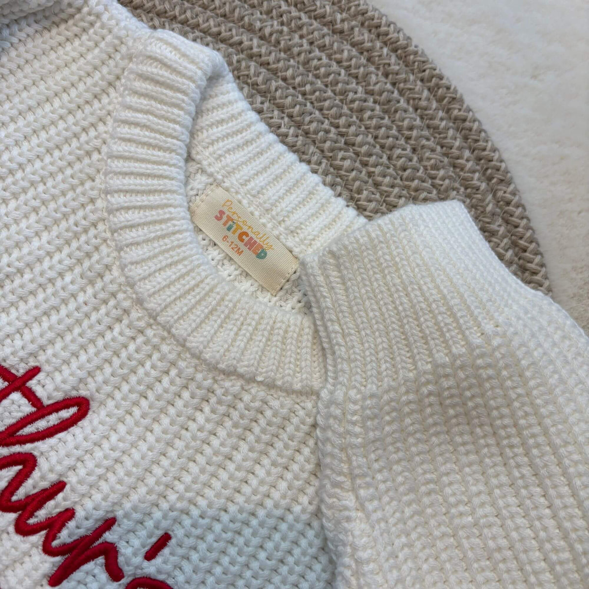 Close-up of a neck label by Personally Stitched on a white-coloured knit romper with red script embroidery on the chest.