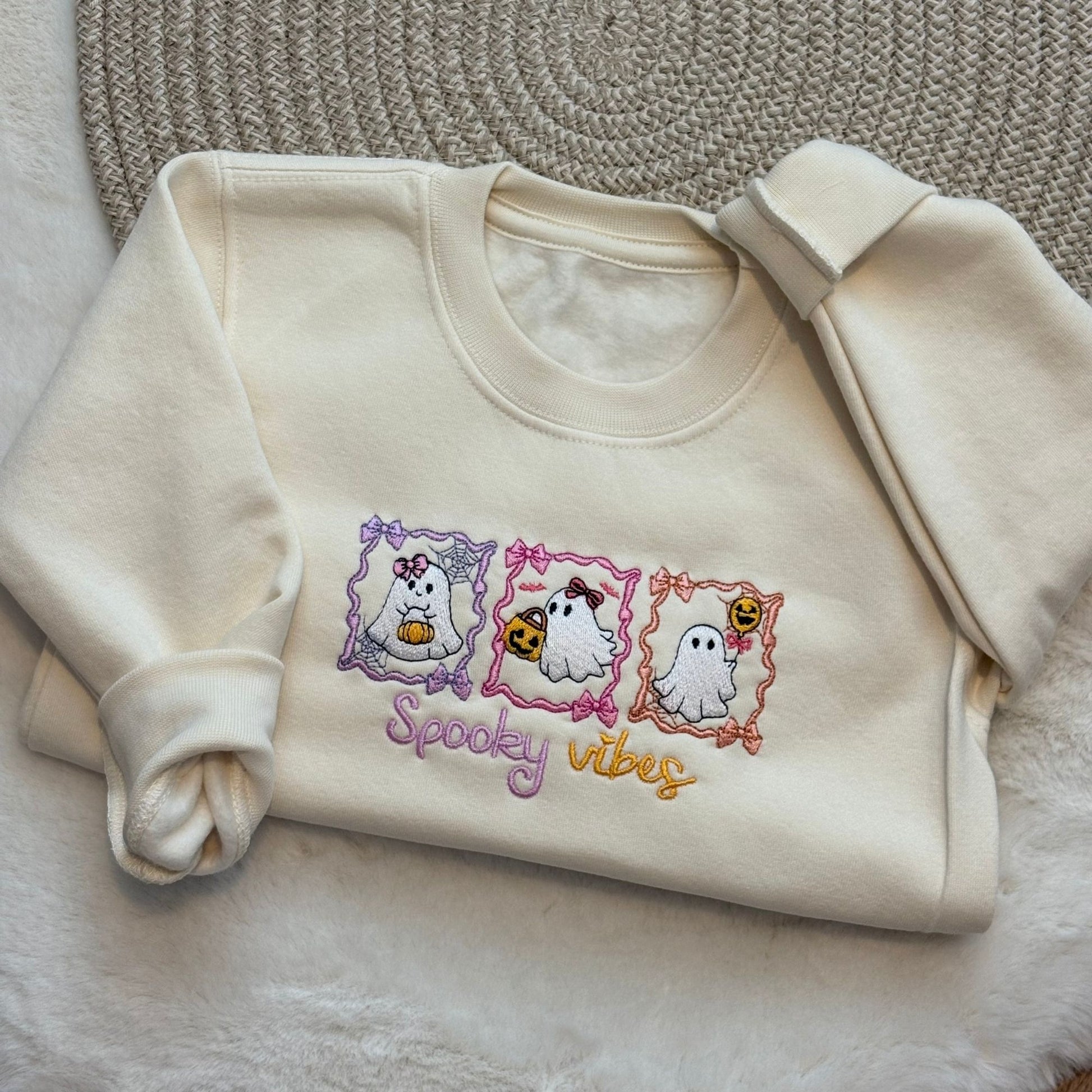 A oat-colored long-sleeve sweatshirt with a 'Spooky vibes' graphic featuring three cute embroidered ghosts in frames.