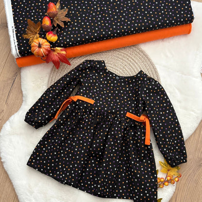 A toddler girl's long-sleeve dress with a black base, white and orange polka dots, and orange ribbon ties at the waist.