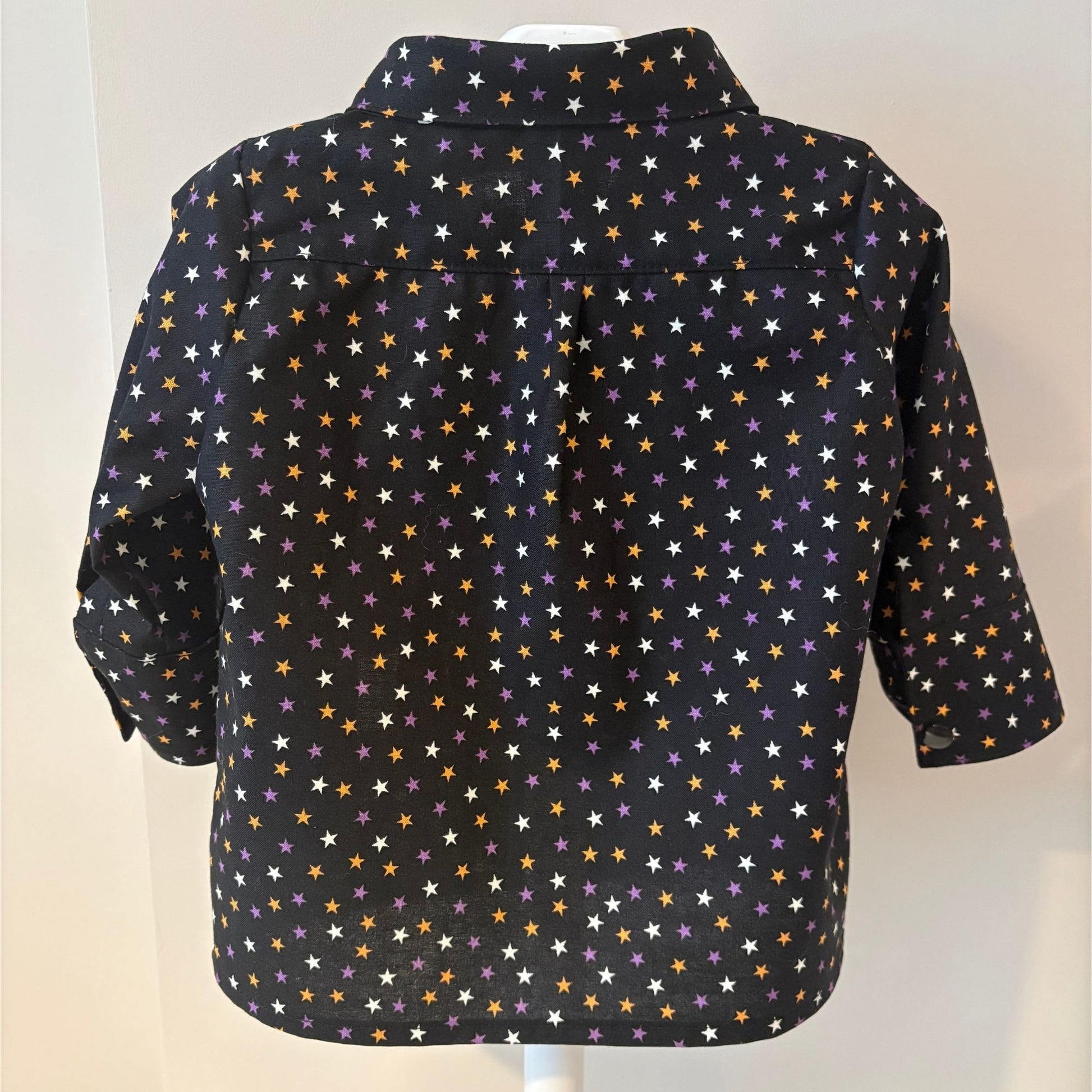 A back view of a long-sleeve shirt with a black base and an all-over pattern of small stars in purple, white, and orange, displayed on hanger