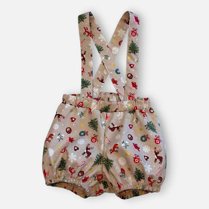 A pair of baby bloomers with adjustable suspenders, featuring a festive Christmas print with reindeer, trees, candy canes, and snowflakes on a light beige background.