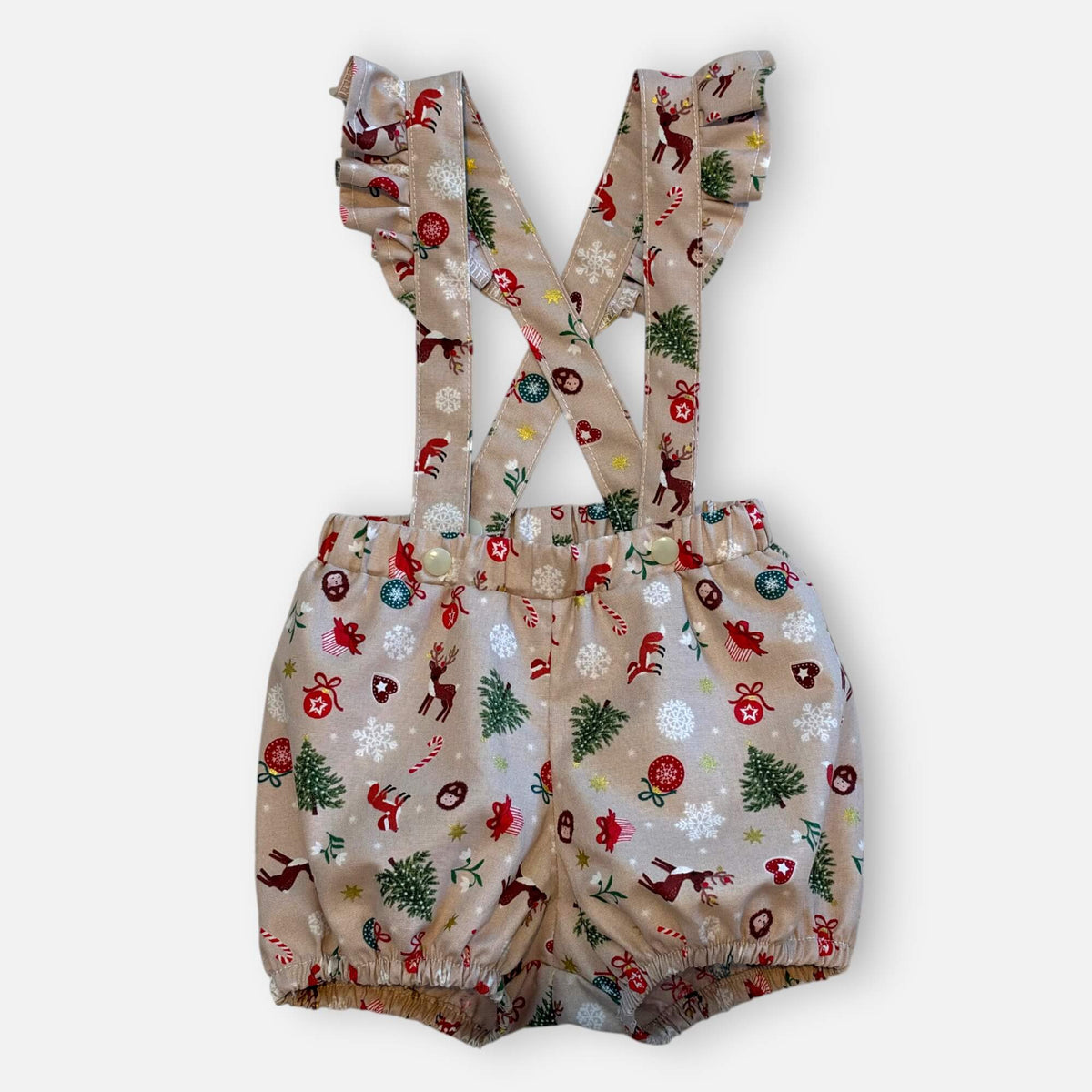 A pair of baby bloomers with frill suspenders, featuring a festive Christmas print with reindeer, trees, candy canes, and snowflakes on a light beige background.