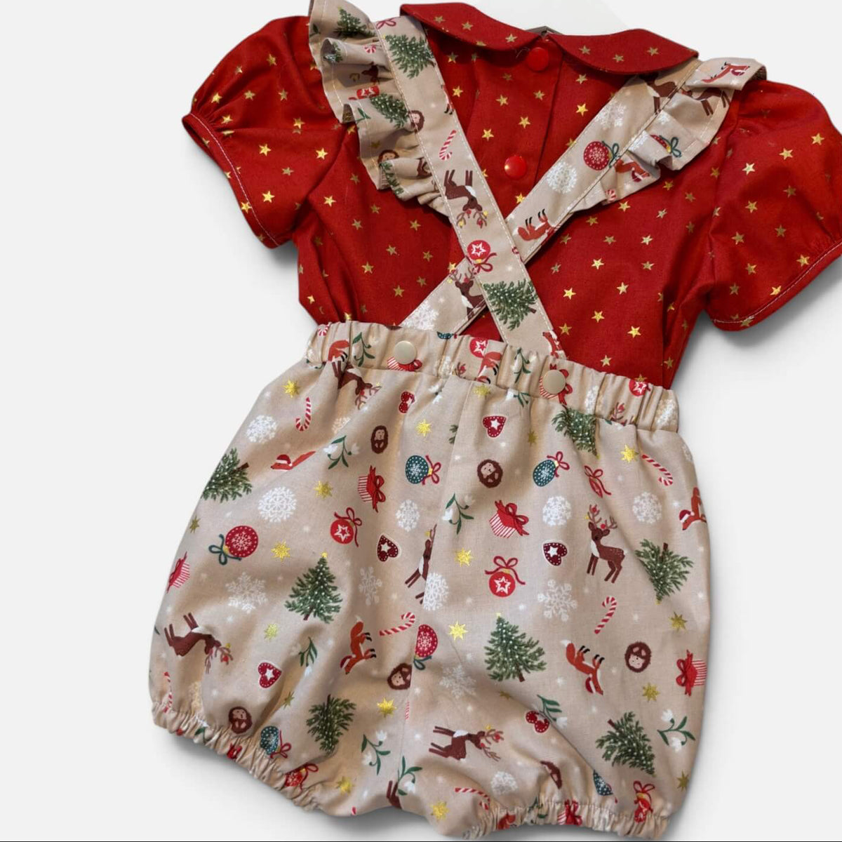 A baby romper with a red short-sleeve top featuring gold stars and a beige bib-style bottom with a Christmas print of trees, candy canes, and reindeer, displayed on a white hanger against a light gray background.