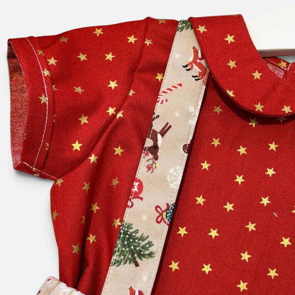 A close-up of a red fabric garment with gold star print, a Peter Pan collar, and a decorative cream ribbon with Christmas illustrations, photographed on a white background.