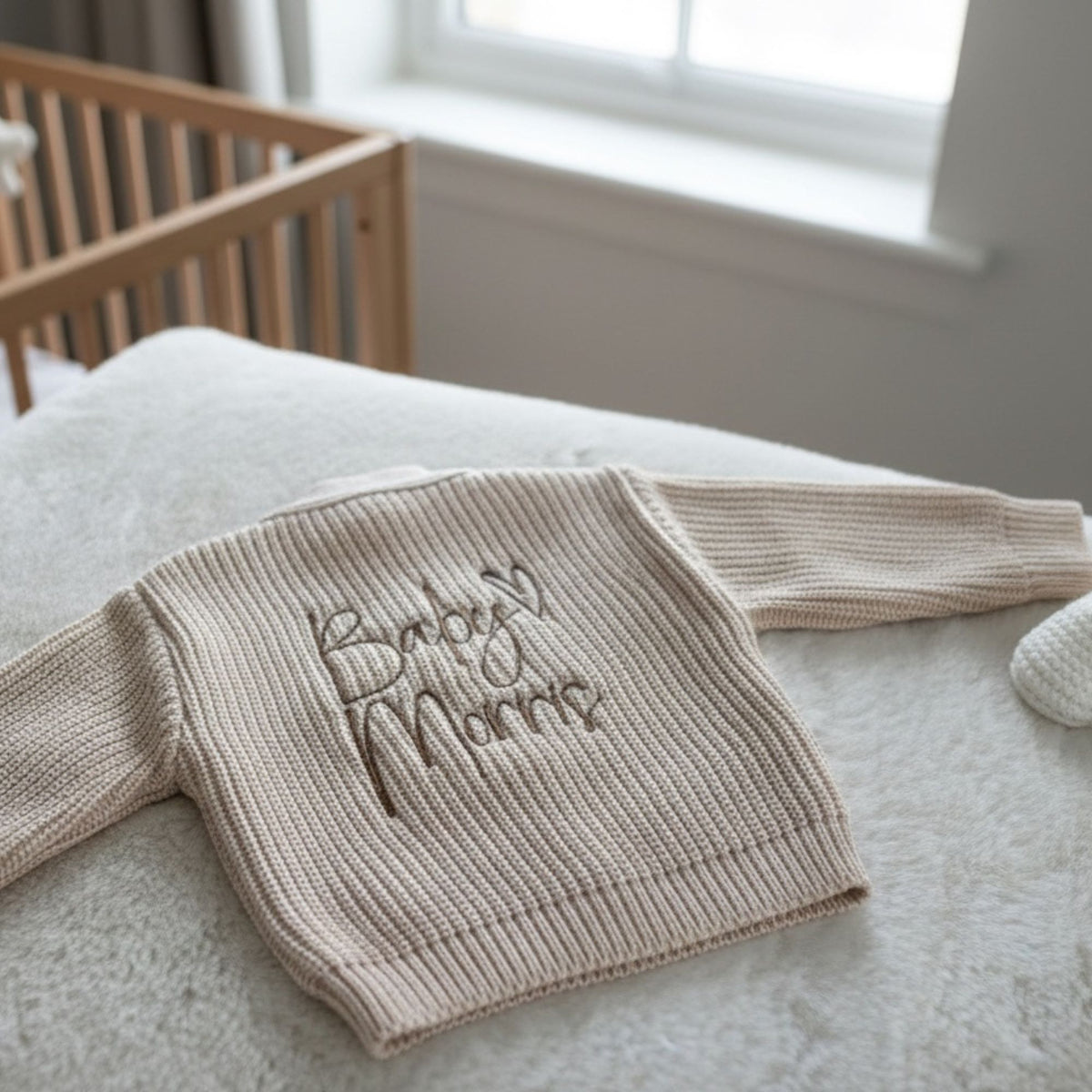 A beige ribbed knit baby cardigan with Baby Surname embroidered on the back in a light brown thread available in 0-3 months up to 12-18 months 