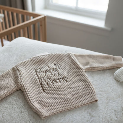 A beige ribbed knit baby cardigan with Baby Surname embroidered on the back in a light brown thread available in 0-3 months up to 12-18 months 