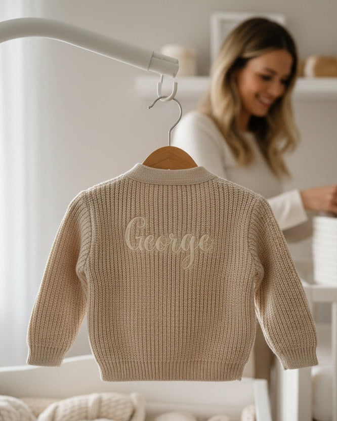 Beige sweater with 'George' embroidered on a hanger in a nursery setting.