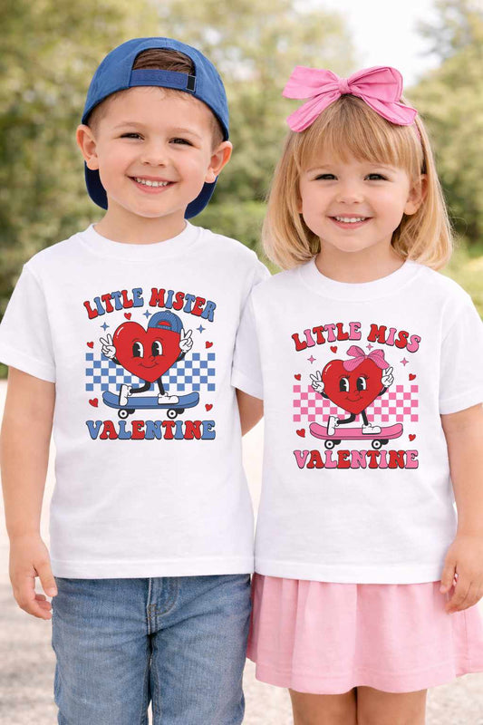 wo white children’s Valentine’s Day T-shirts hanging on a wooden rail featuring Little Mister and Little Miss Valentine designs